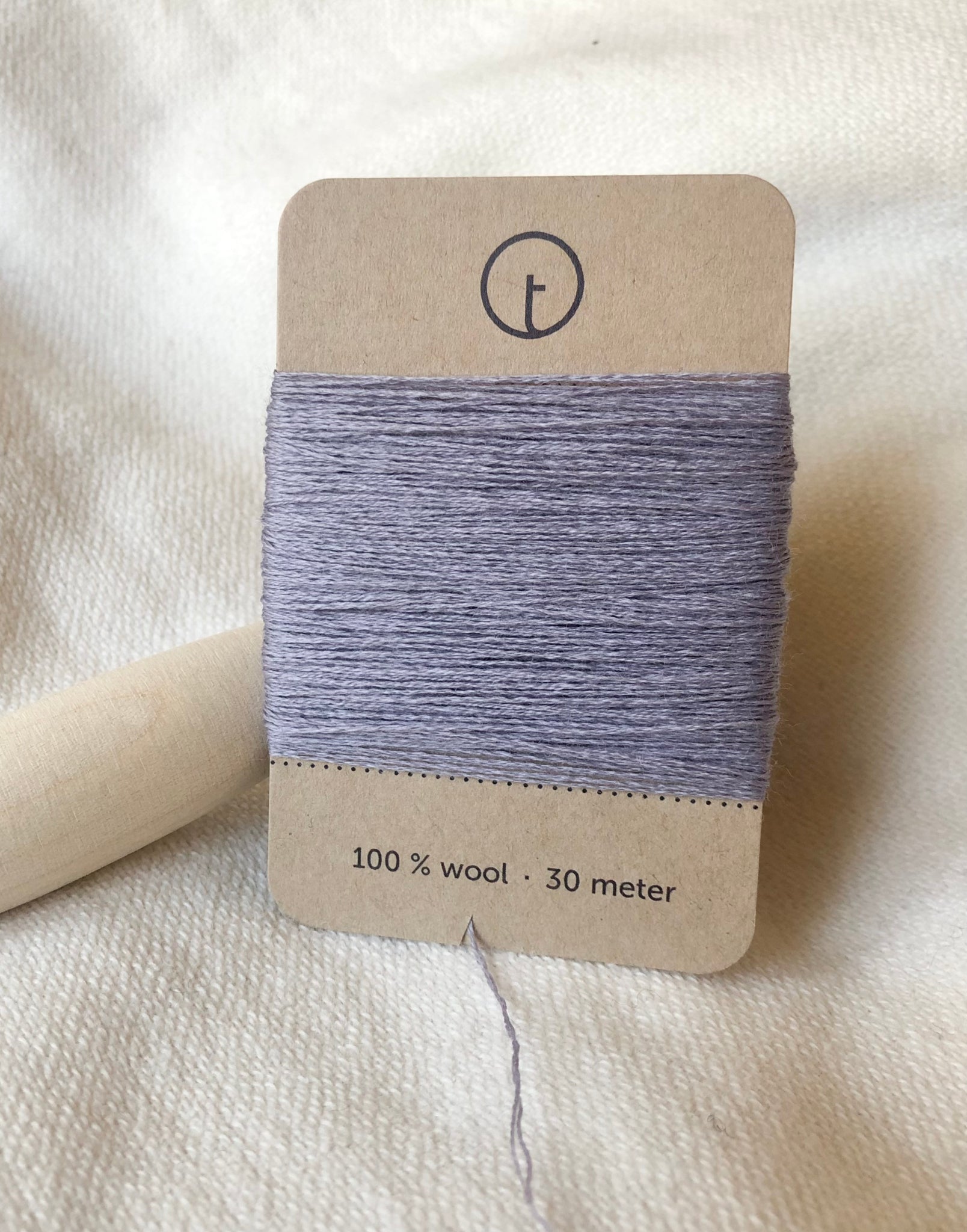 A 30-meter card of 100% wool darning yarn in light purple colour neatly wrapped around a labeled rectangular paper card, ideal for repairing knitwear.