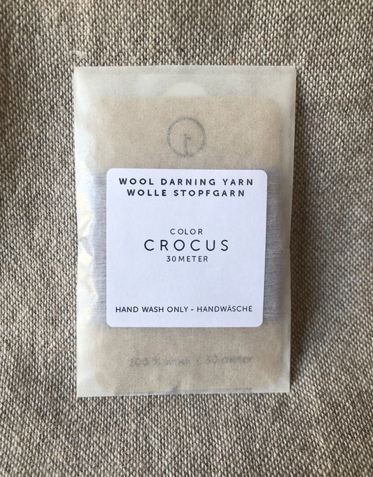 A 30-meter card of 100% wool darning yarn in light purple colour, neatly wound and ready for mending knit garments. The yarn is packaged in a small, eco-friendly parchment paper bag.