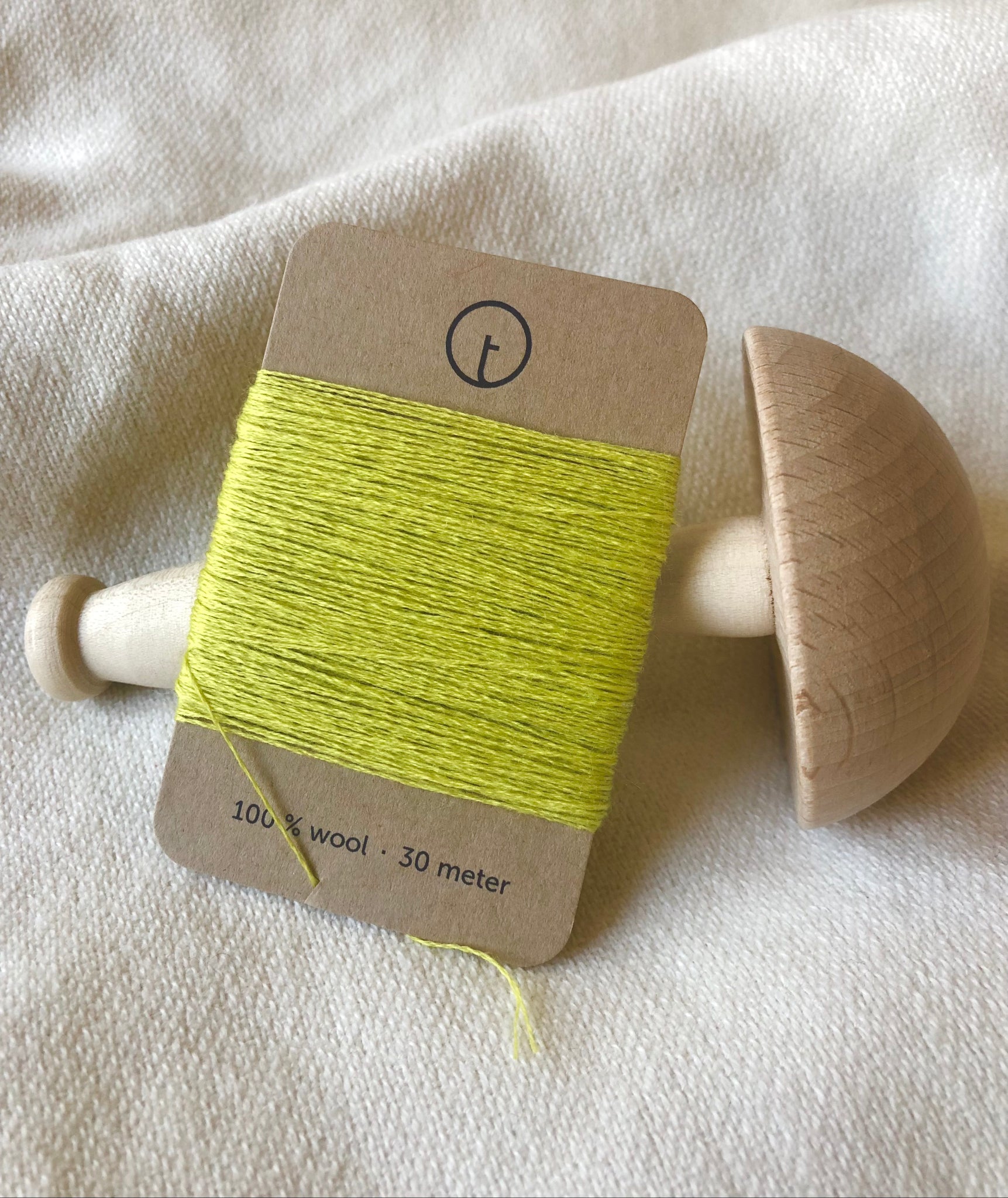A 30-meter card of 100% wool darning yarn in light yellow lemon color neatly wrapped around a labeled rectangular paper card, ideal for repairing knitwear.