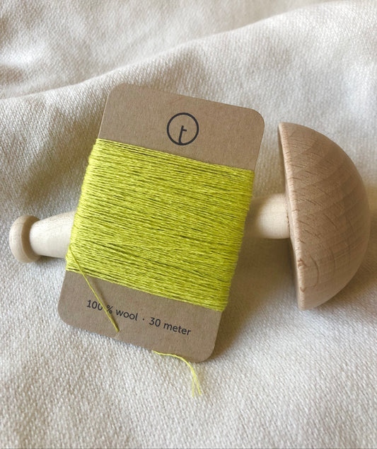 A 30-meter card of 100% wool darning yarn in light yellow lemon color neatly wrapped around a labeled rectangular paper card, ideal for repairing knitwear.