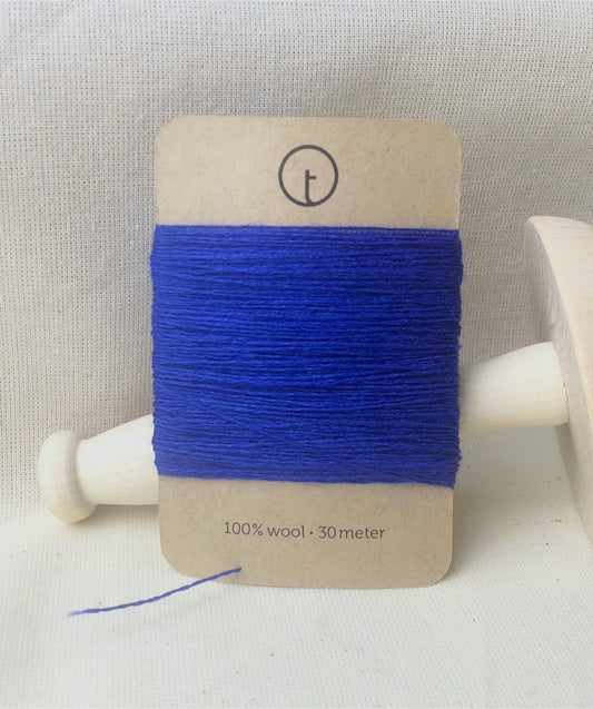 A 30-meter card of 100% wool darning yarn in New Blue (bright blue color) neatly wrapped around a labeled rectangular paper card, ideal for repairing knitwear.