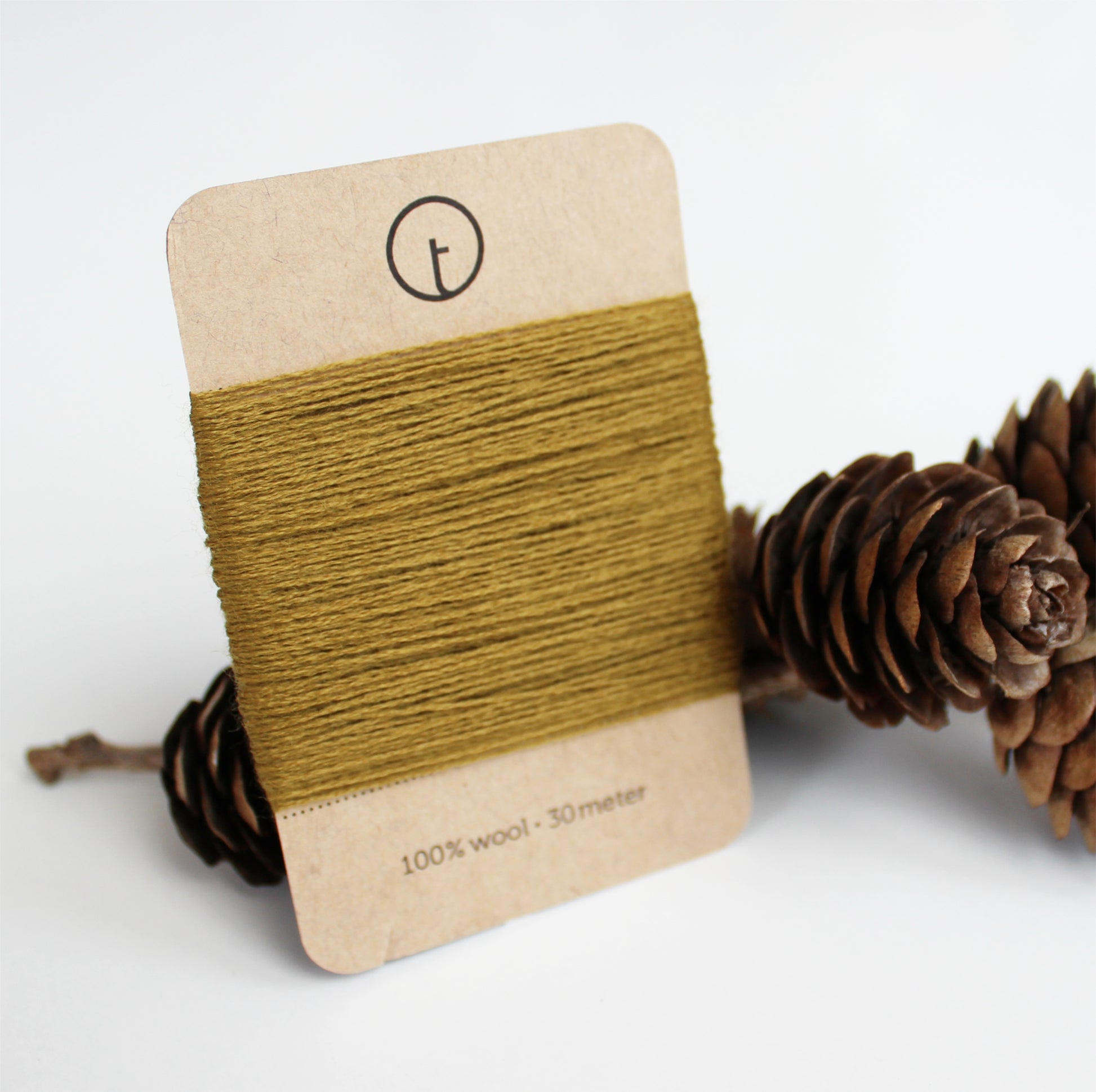 A 30-meter card of 100% wool fine darning yarn in mustard colour, neatly wrapped around a labeled rectangular paper card, ideal for repairing knitwear.
