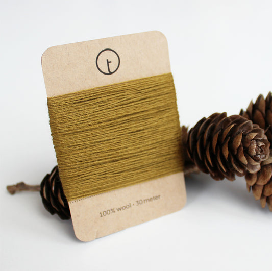 A 30-meter card of 100% wool fine darning yarn in mustard colour, neatly wrapped around a labeled rectangular paper card, ideal for repairing knitwear.