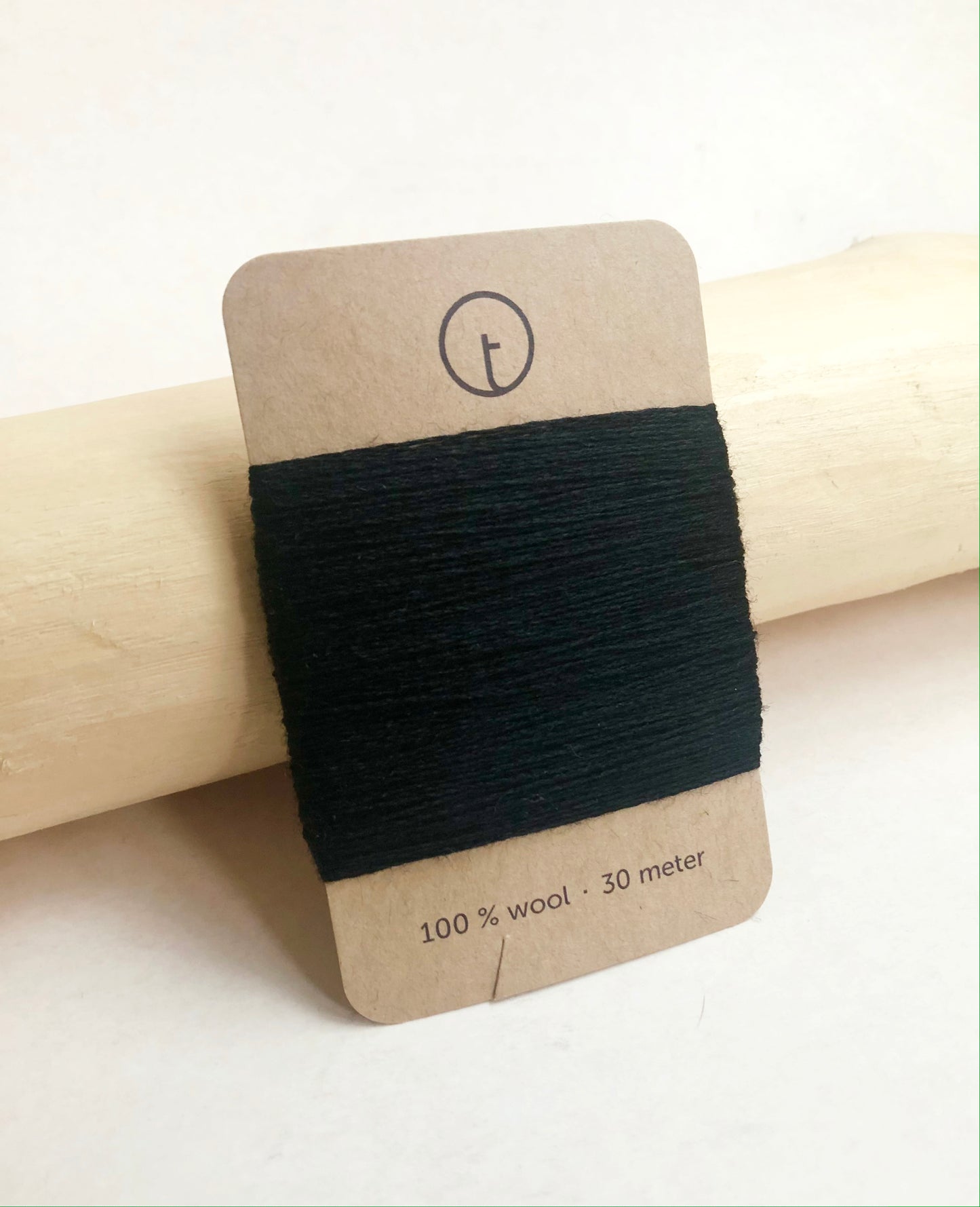 A 30-meter card of 100% wool darning yarn in black colour, neatly wrapped around a labeled rectangular paper card, ideal for repairing knitwear.