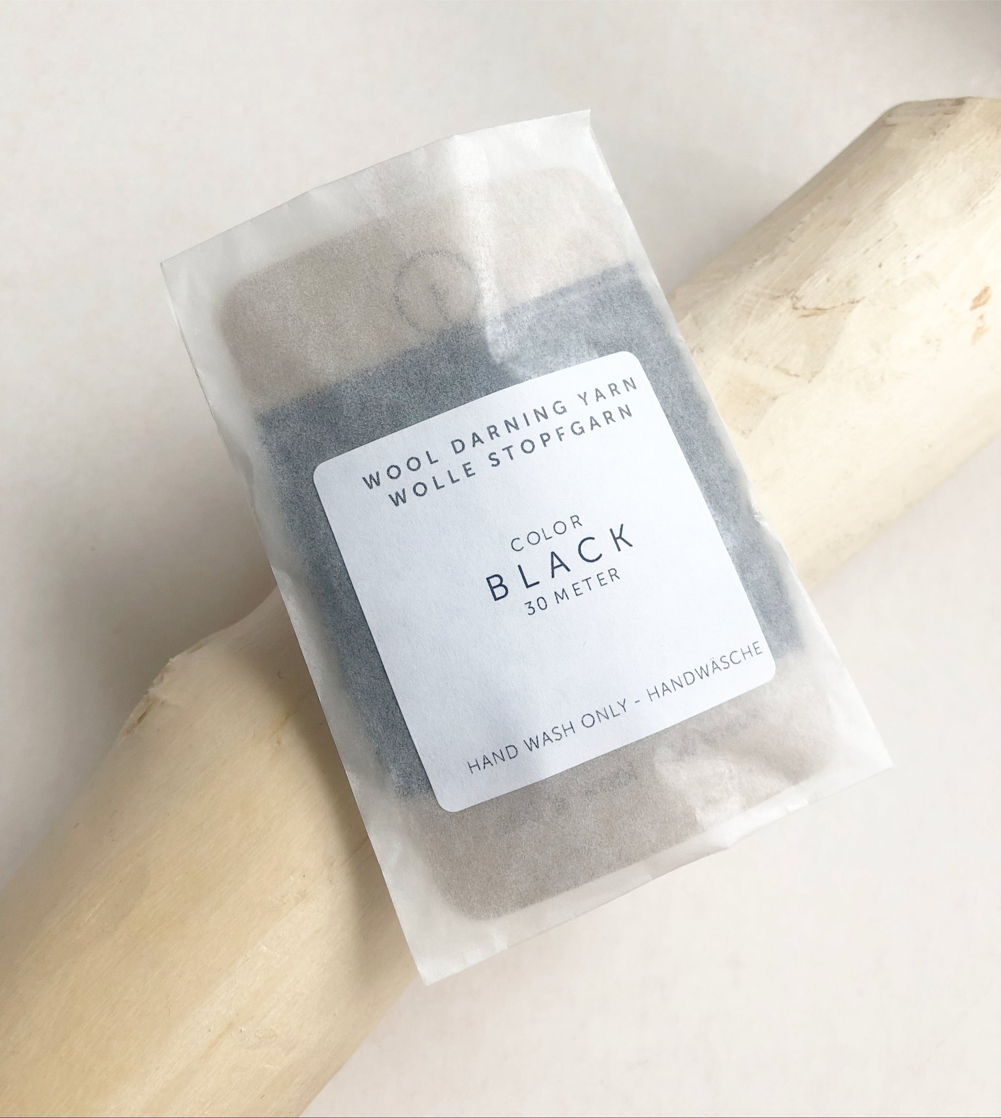 A 30-meter card of 100% wool darning yarn in black colour, neatly wound and ready for mending knit garments. The yarn is packaged in a small, eco-friendly parchment paper bag.
