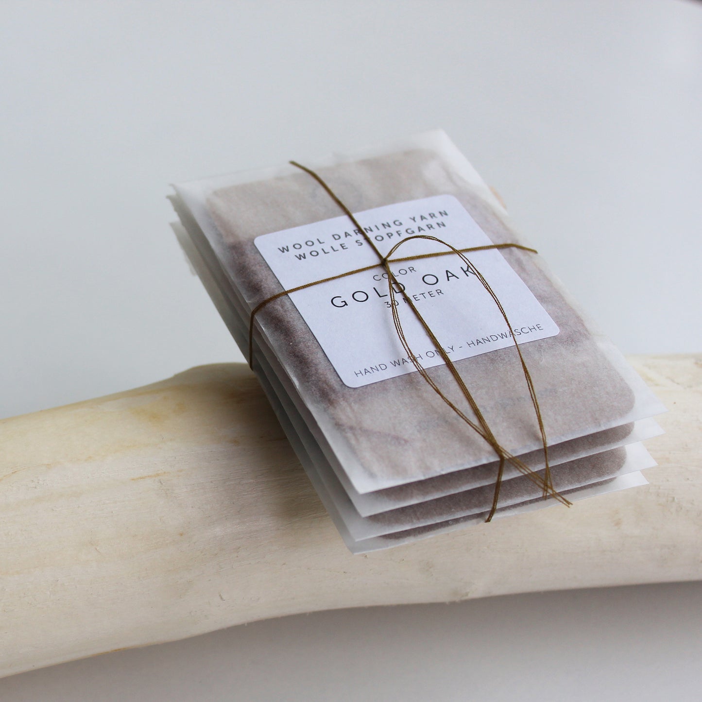 A pack of four 30-meter cards of 100% wool darning yarn in assorted colors. The yarn cards are enclosed in a small, eco-friendly parchment paper bag, ideal for mending socks, sweaters, and other wool garments.