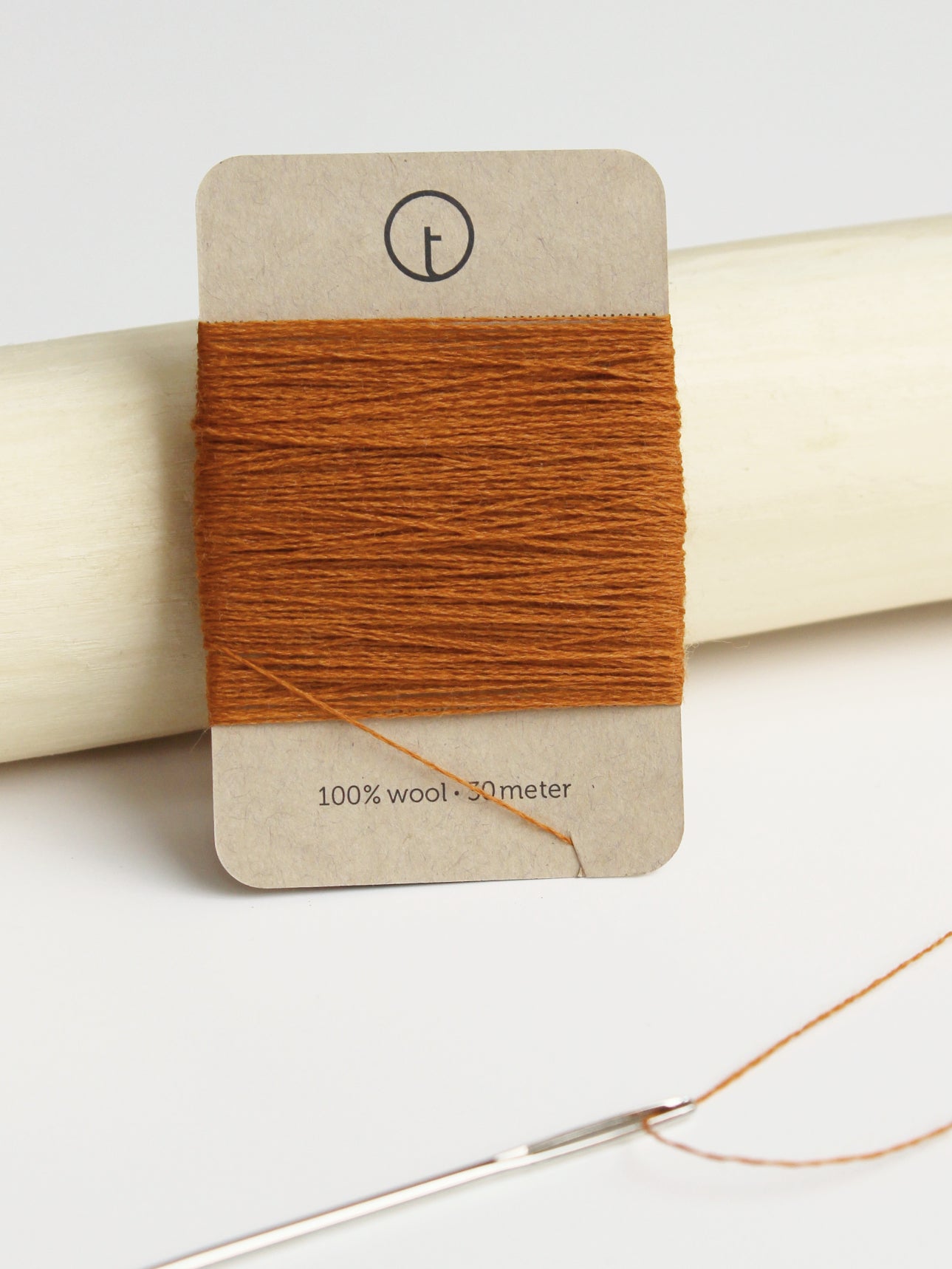 A 30-meter card of 100% wool fine darning yarn in cinnamon (dark orange) colour, neatly wrapped around a labeled rectangular paper card, ideal for repairing knitwear.