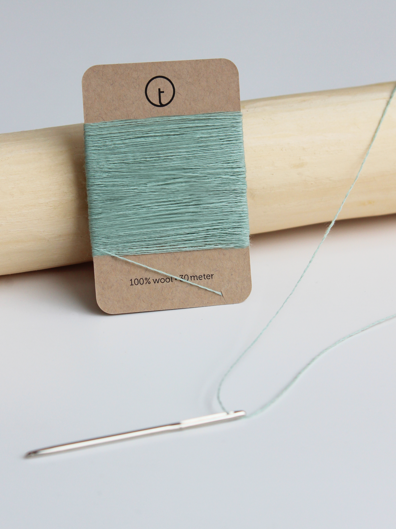 A 30-meter card of 100% wool fine darning yarn in mint colour, neatly wrapped around a labeled rectangular paper card, ideal for repairing knitwear.