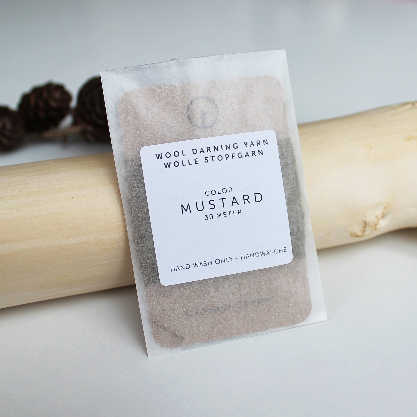 A 30-meter card of 100% wool darning yarn in mustard colour, neatly wound and ready for mending knit garments. The yarn is packaged in a small, eco-friendly parchment paper bag.