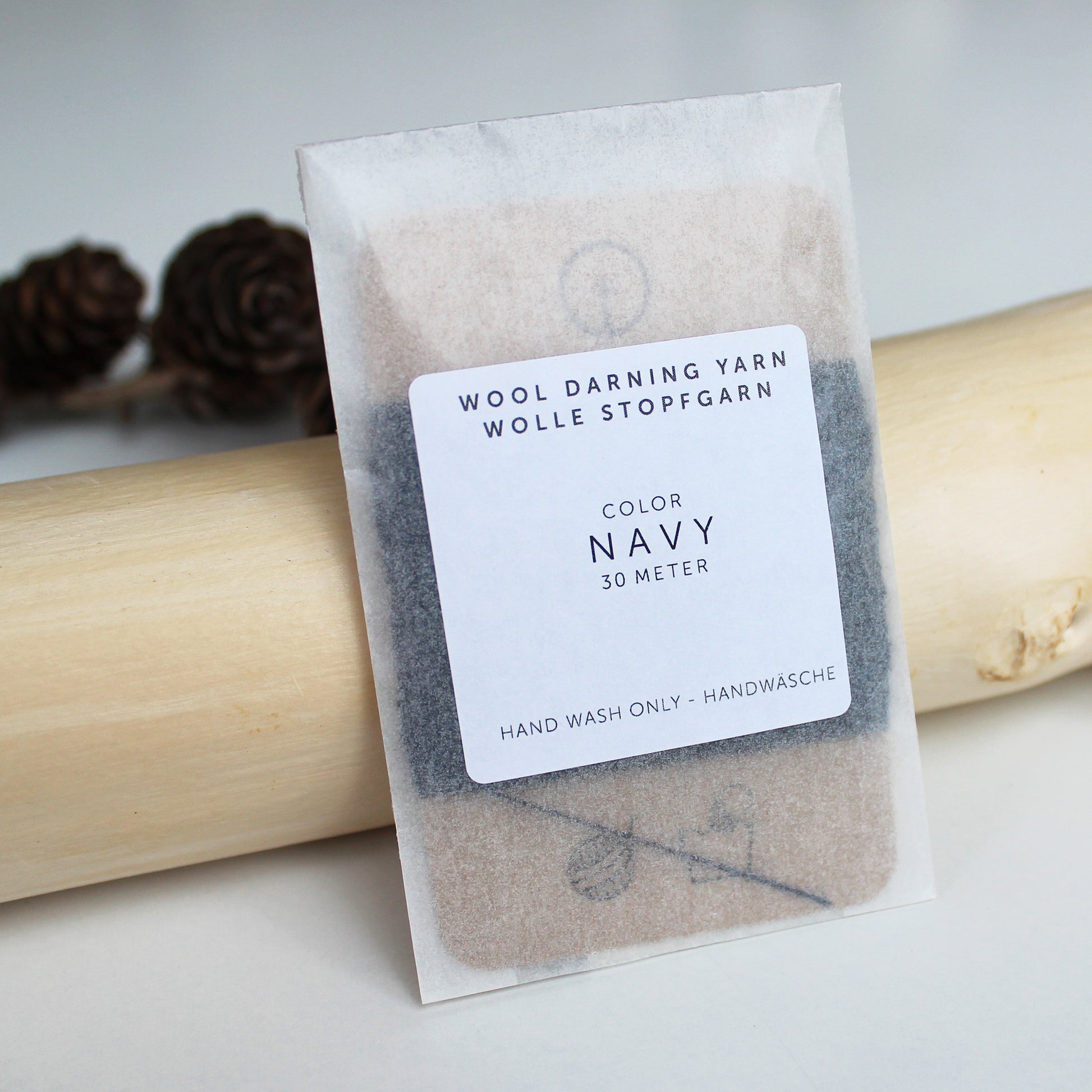 A 30-meter card of 100% wool darning yarn in Navy (darn blue) colour, neatly wound and ready for mending knit garments. The yarn is packaged in a small, eco-friendly parchment paper bag.