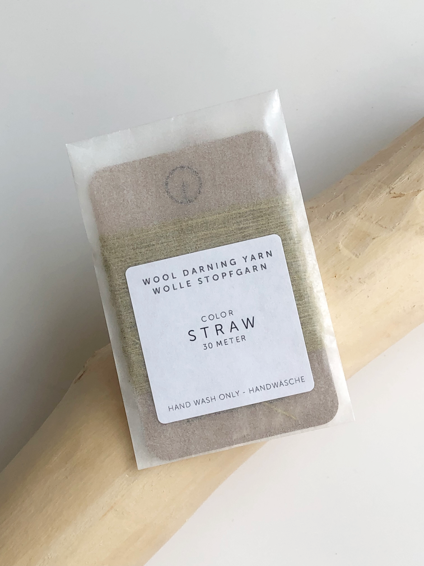 A 30-meter card of 100% wool darning yarn in straw (golden yellow) colour, neatly wound and ready for mending knit garments. The yarn is packaged in a small, eco-friendly parchment paper bag.