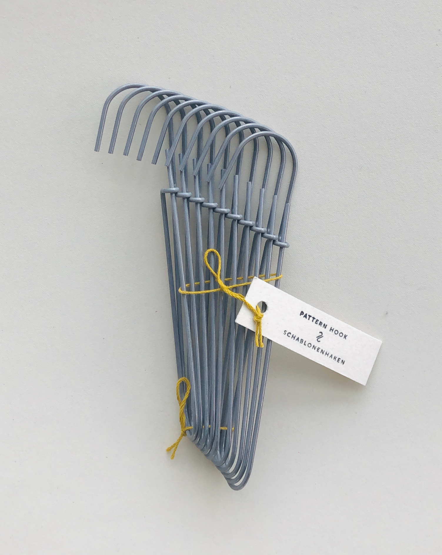 Set of 10 heavy-duty steel wire hooks in two sizes: large (18 cm long, 12.5 cm loop, 3.5 cm wide) and small (11.5 cm long, 8.5 cm loop, 2 cm wide). Made in Germany, designed for organizing patterns, tools, and scissors. Plastic-free with a spring-clip loop. Matte, powdery finish that becomes smooth over time.