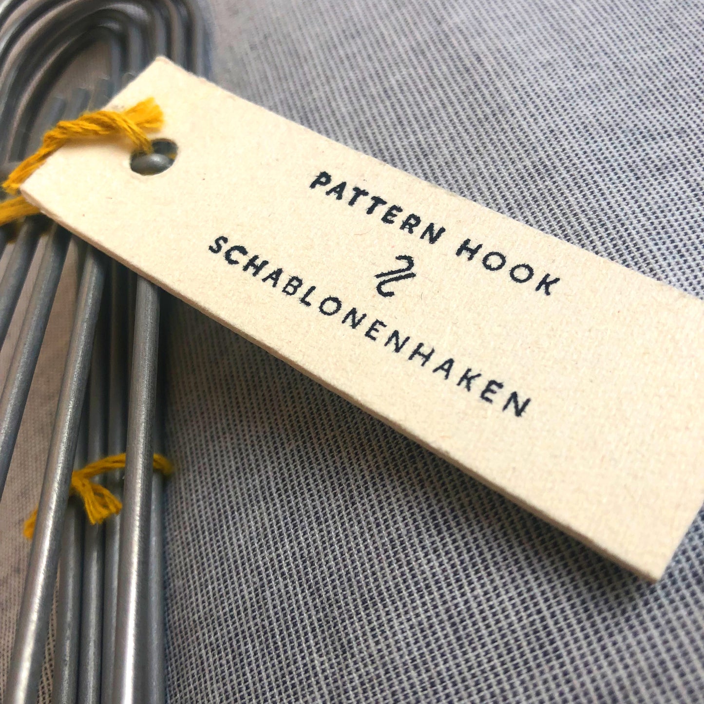 A label for heavy-duty steel wire hooks in two sizes: large (18 cm long, 12.5 cm loop, 3.5 cm wide) and small (11.5 cm long, 8.5 cm loop, 2 cm wide). Made in Germany, designed for organizing patterns, tools, and scissors. Plastic-free with a spring-clip loop. Matte, powdery finish that becomes smooth over time.